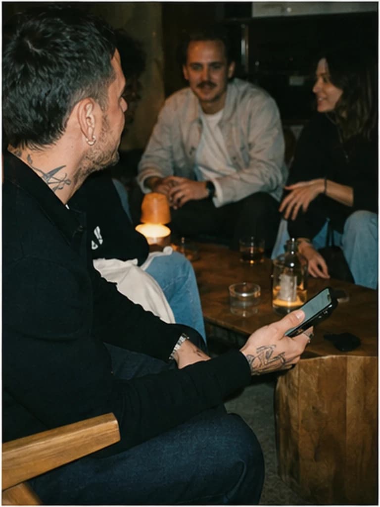 Founder holding a phone in a lounge while friends talk in the background