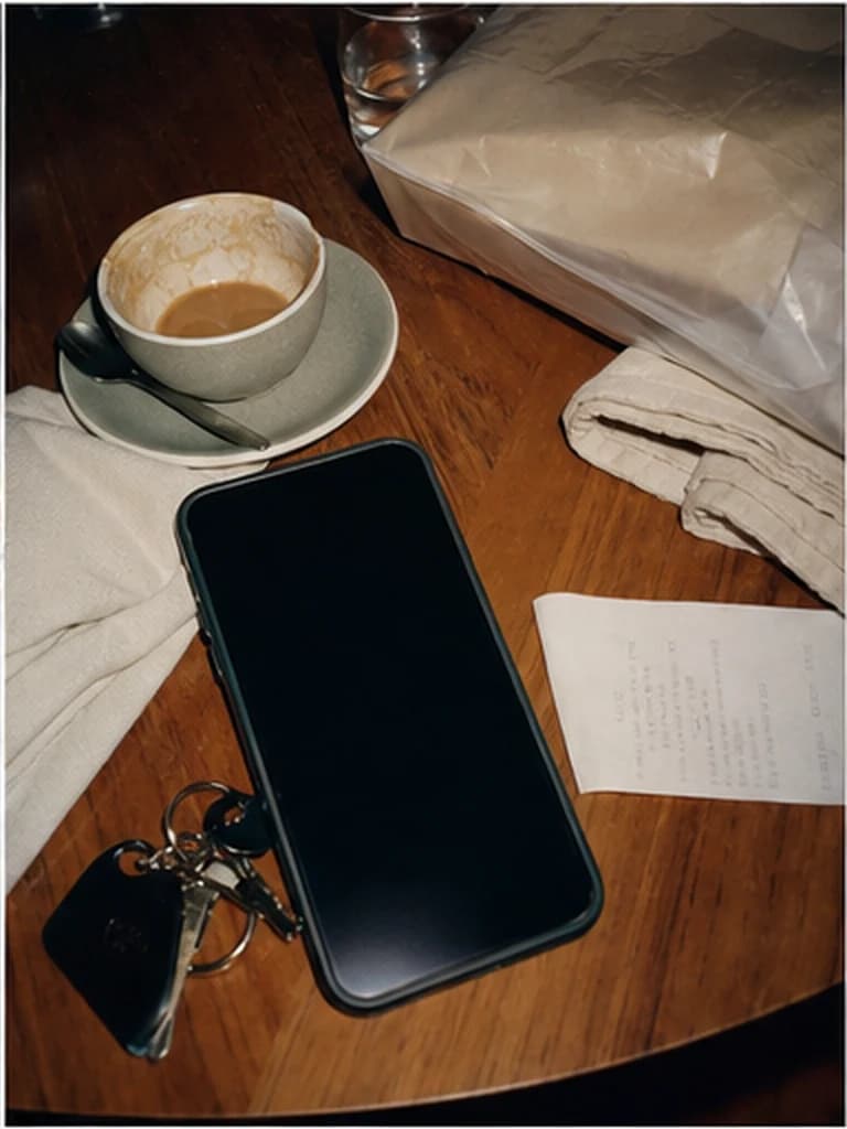 Phone beside coffee, notes and a soft parcel bag on a warm table