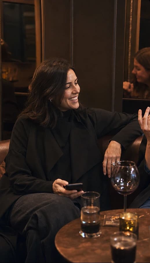 Founder laughing with friends in a warm lounge while holding her phone