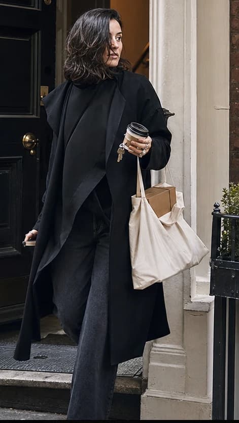 Female founder stepping through a doorway with a phone, coffee and unbranded tote